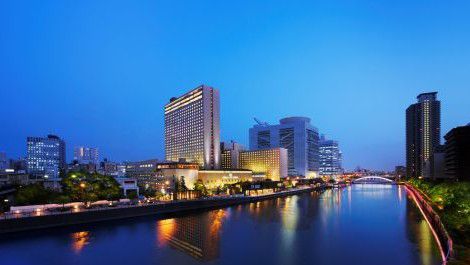 City buildings illuminated along a calm river at dusk