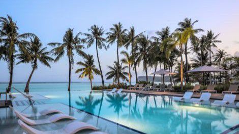 Resort pool surrounded by palm trees overlooking a calm ocean at sunset