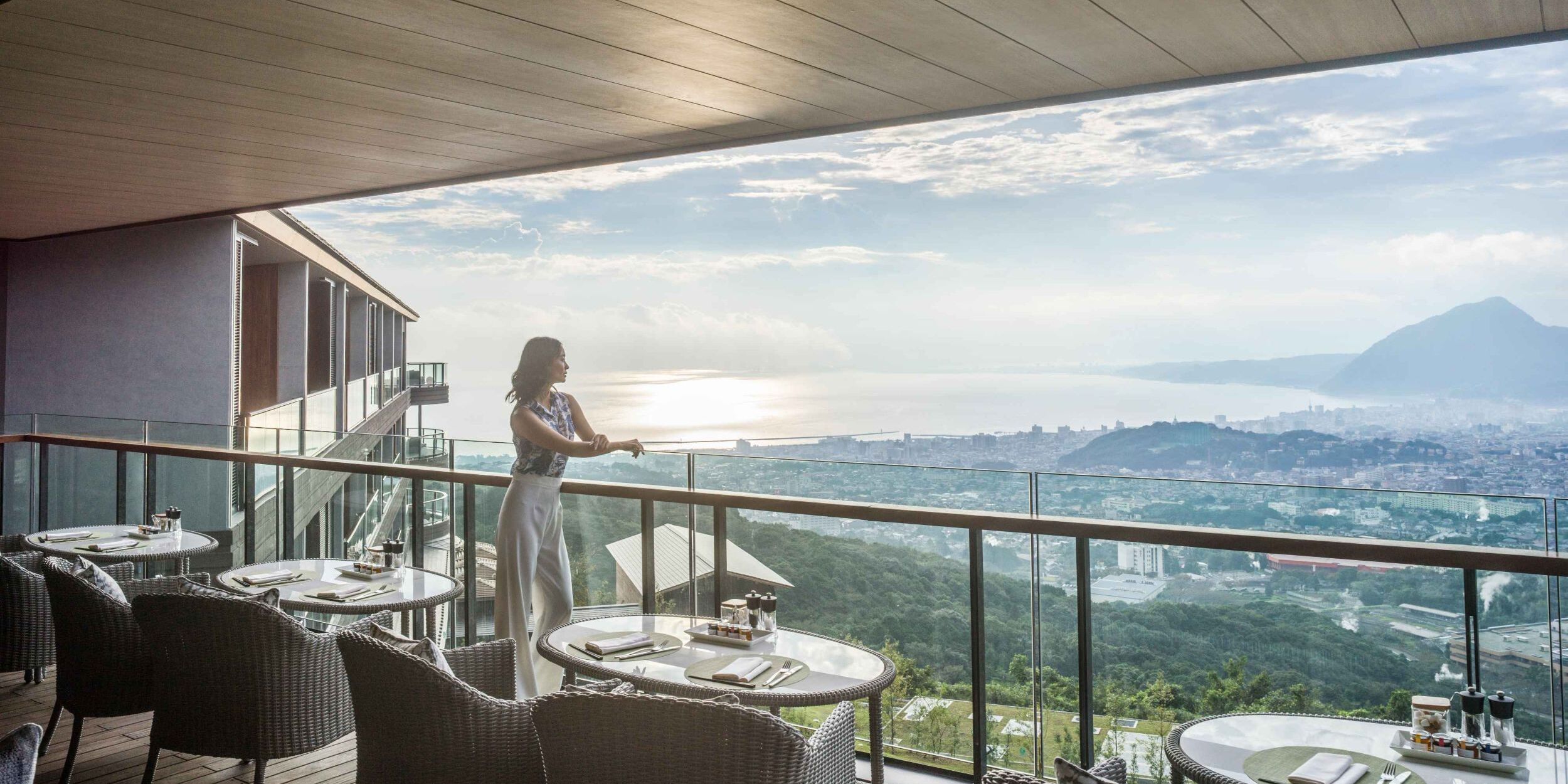 A woman on a terrace overlooking a coastal city and mountains.