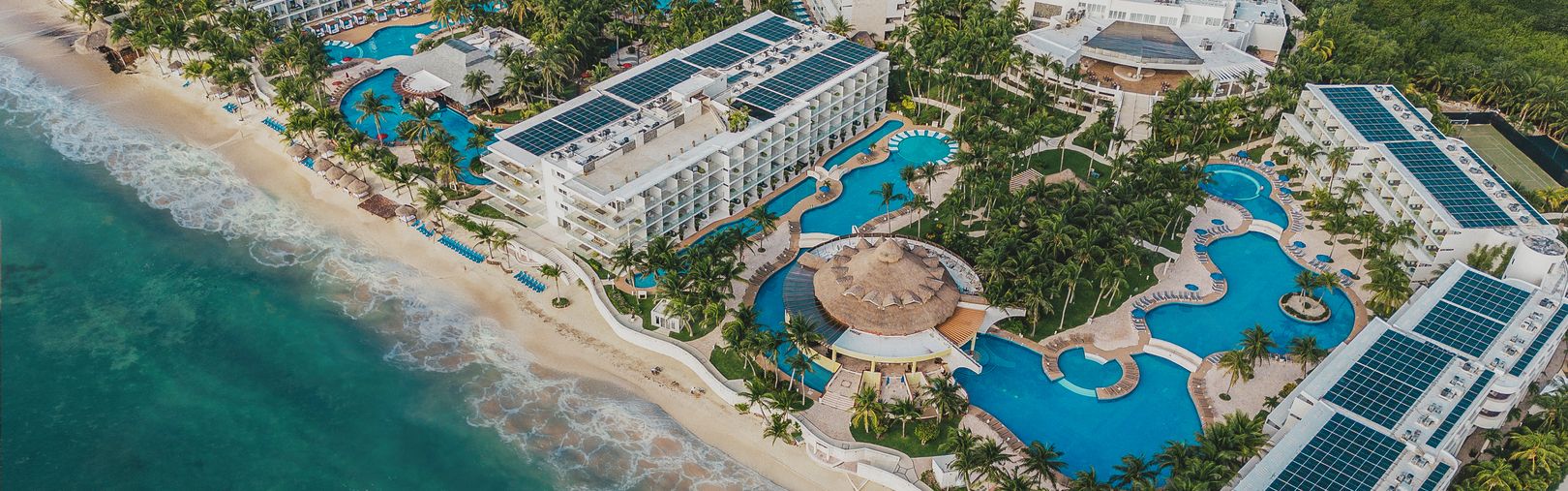 Vue aérienne d'un complexe en bord de mer avec piscines et palmiers.