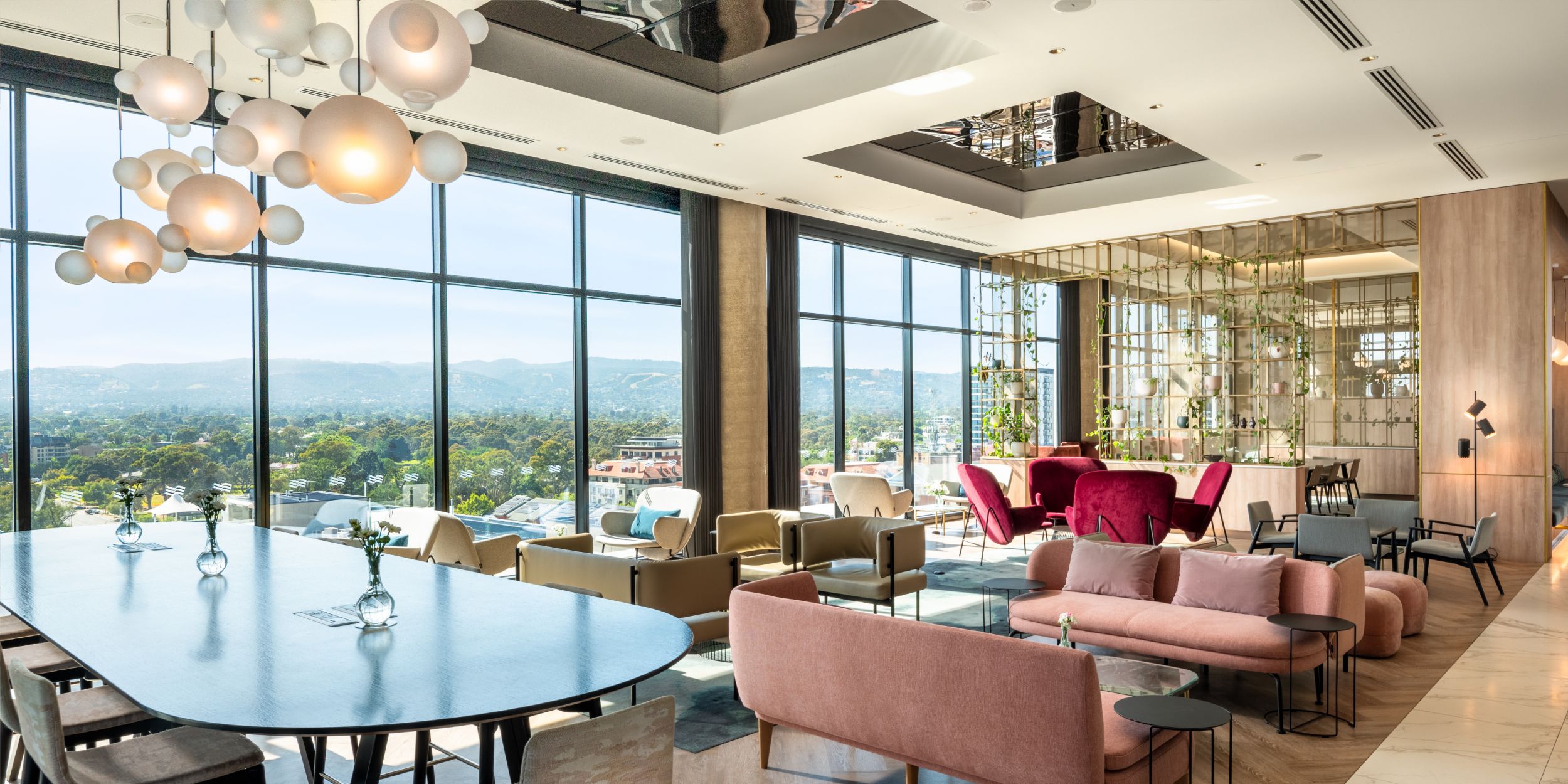 Crowne Plaza Adelaide lounge featuring stylish pink sofas, burgundy chairs, and panoramic skyline windows.