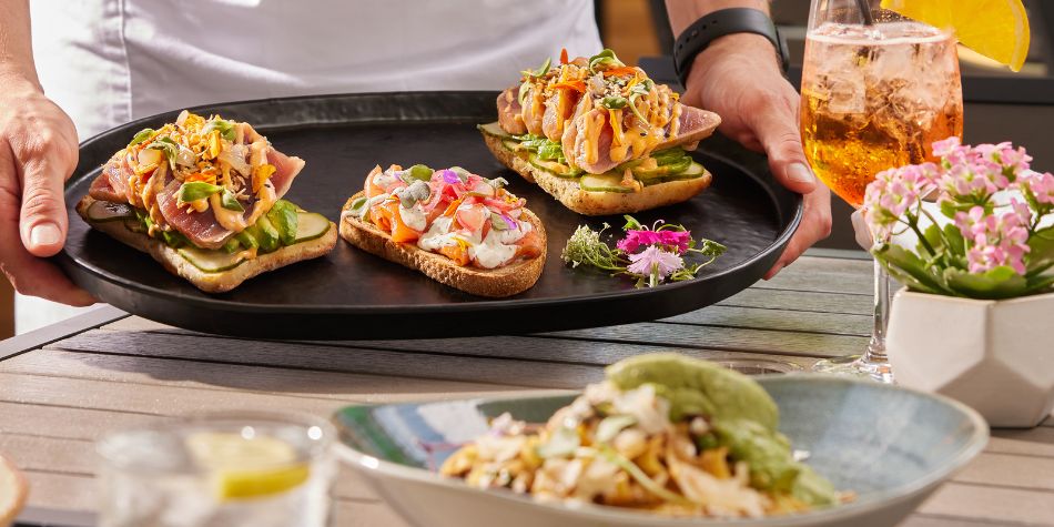 Server presenting gourmet appetizers with cocktail on patio