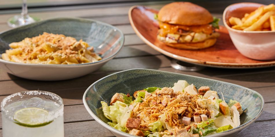Salad, pasta, burger, and drinks served on patio table.