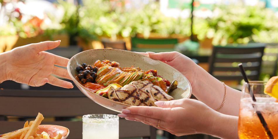Grilled chicken bowl passed across outdoor dining table.