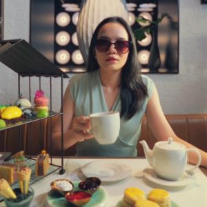 Woman wearing sunglasses holding a cup indoors.