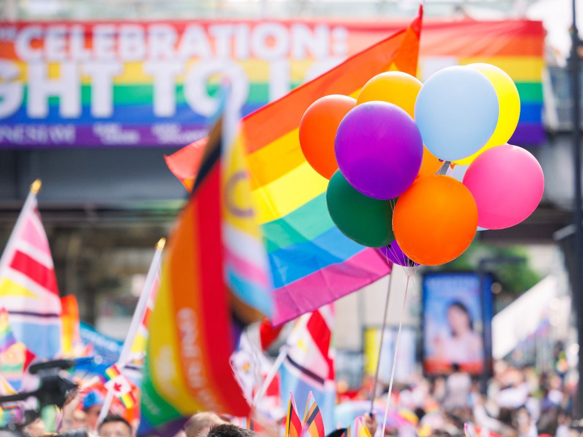 Colorful pride parade featuring rainbow flags, balloons, and a festive crowd.