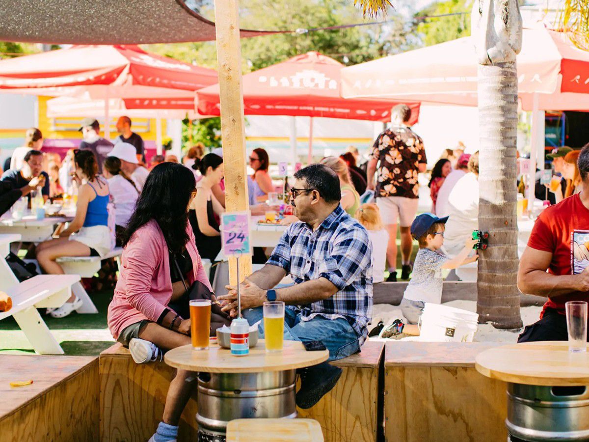 Outdoor brewery dining area with people seated under umbrellas.