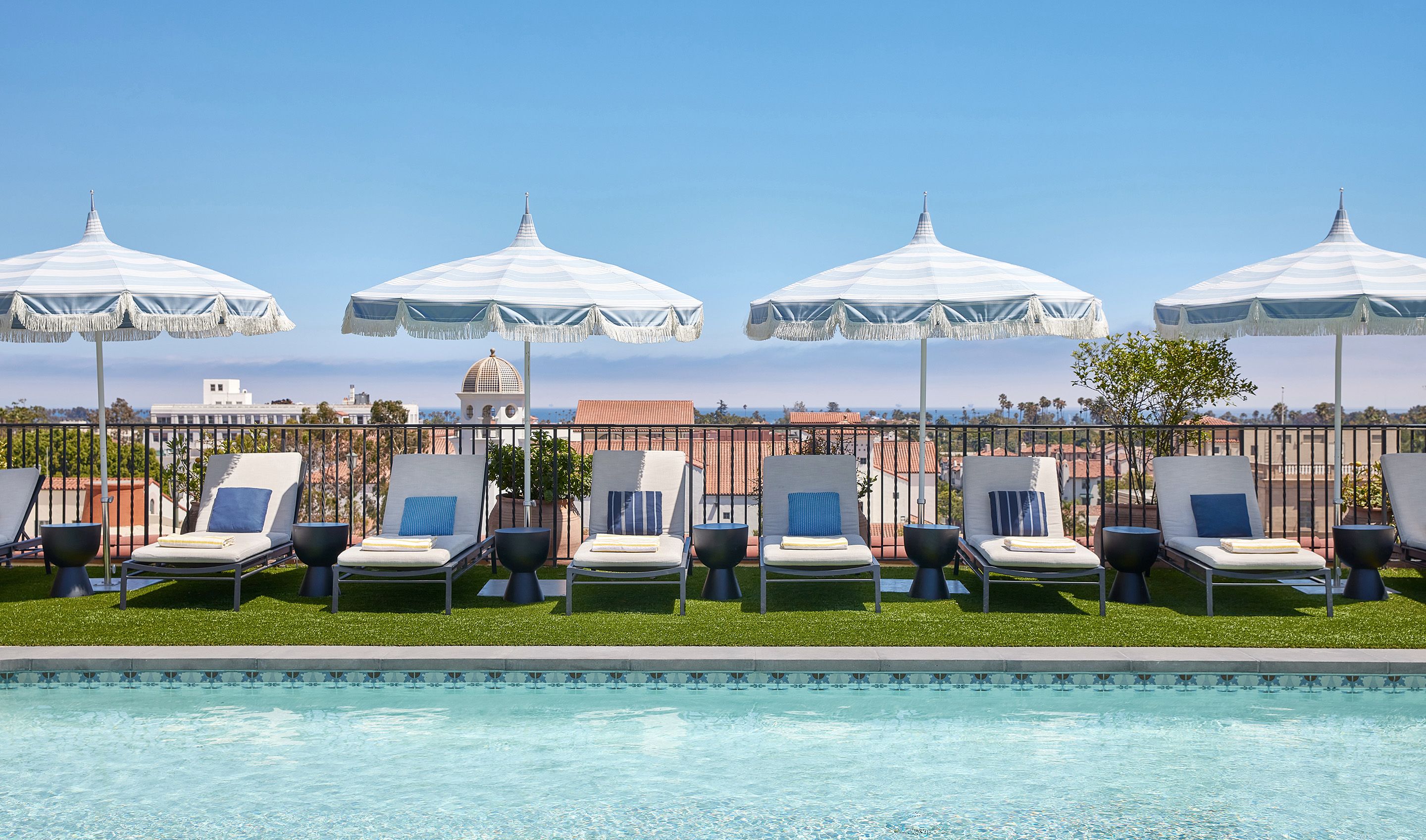 rooftop pool wit a row of lounge chairs and umbrellas overlooking santa barbara