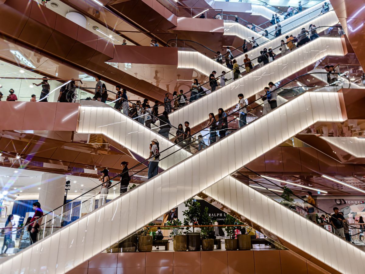 Modern shopping mall interior with illuminated escalators and bustling visitors.
