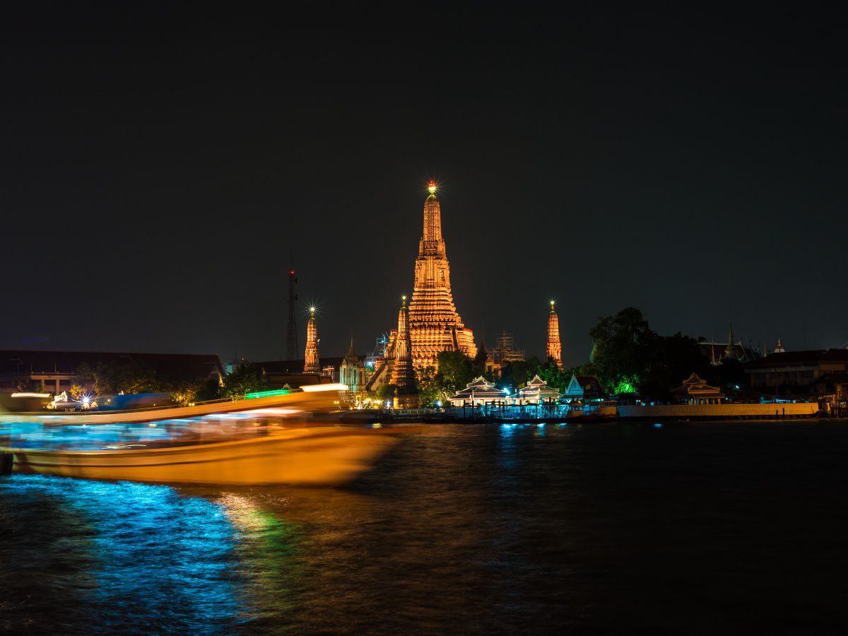 Illuminated riverside temple viewed across the water at night.