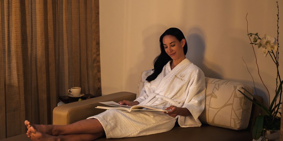 Spa guest reading in robe with tea in tranquil lounge