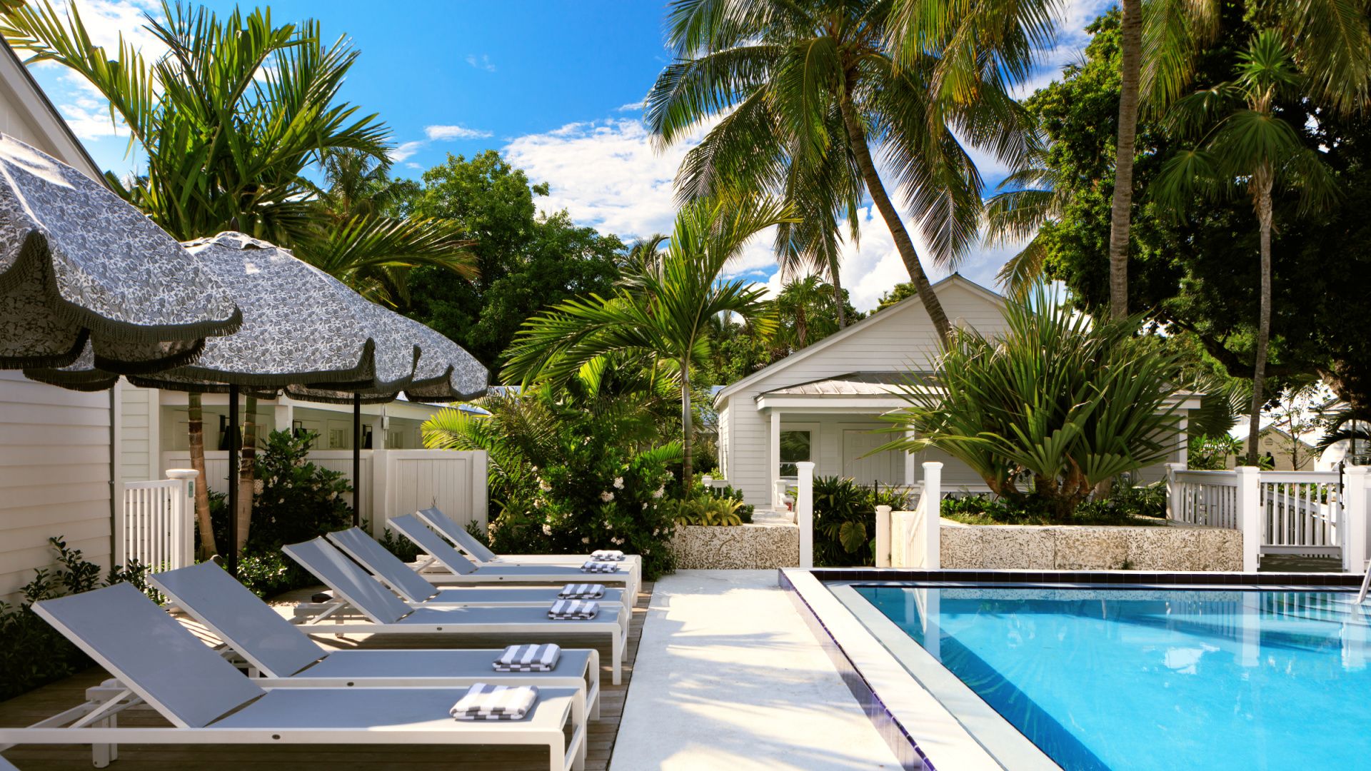 swimming pool with umbrellas and lounge chairs in white and blue in key west