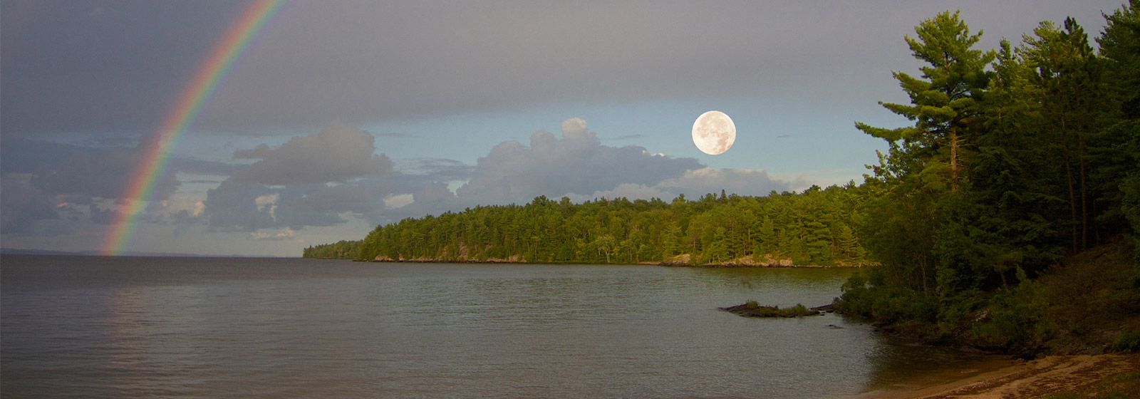 Waters of North Bay coastline, with the moon setting and a rainbow over the moon.