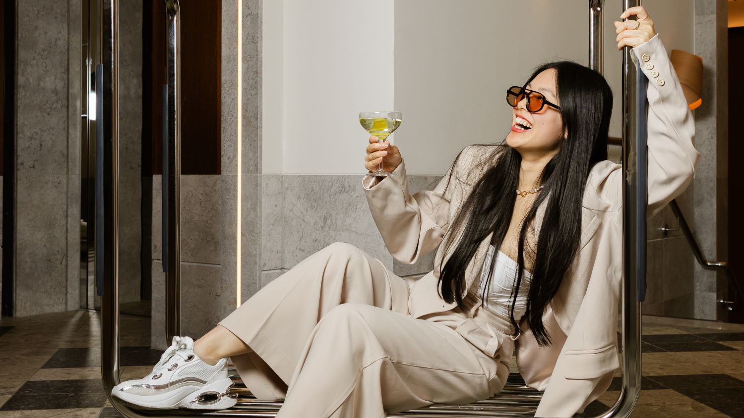 Girl drinking a cocktail whilst sitting on a hotel suitcase roller rack