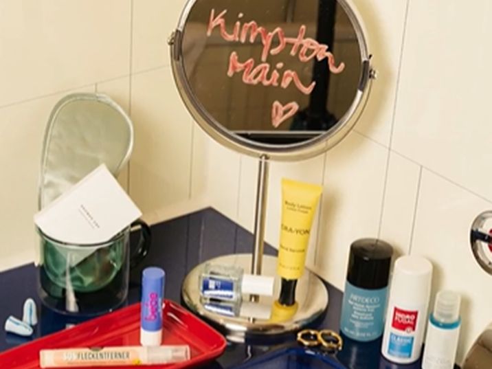 Products surrounding bathroom sink with Kimpton Main lipstick on mirror