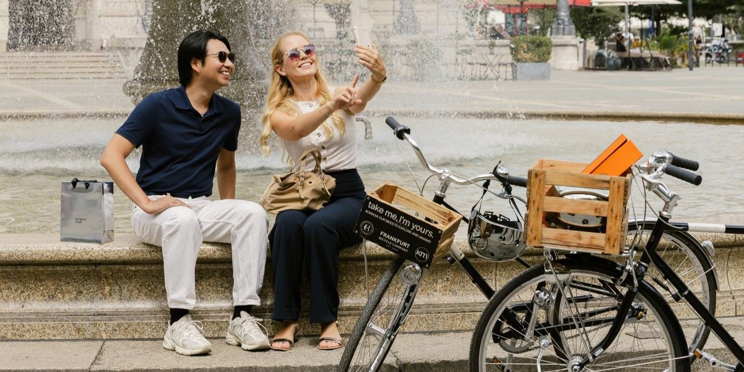 Pärchen, das Frankfurt auf Leihfahrrädern erkunden und Selfies an einem Brunnen machen