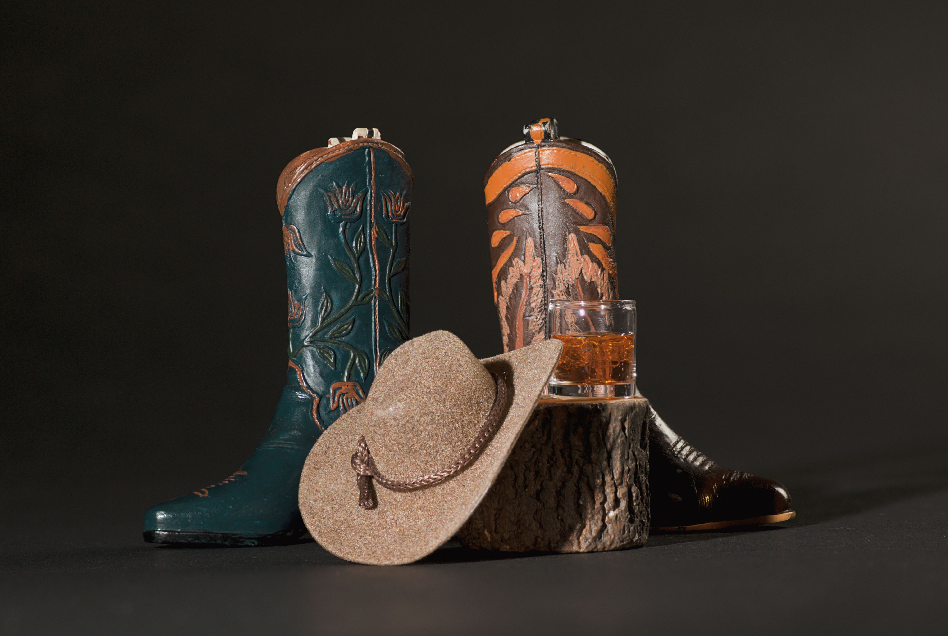Blue and Tan Cowboy Boots, Whiskey, Animal Skull, Cowboy Hat and Lasso Rope on a Tree Stump