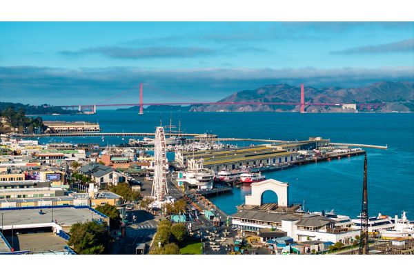 This aerial view captures the vibrant Fisherman's Wharf area in San Francisco, with the iconic Golden Gate Bridge visible in the background