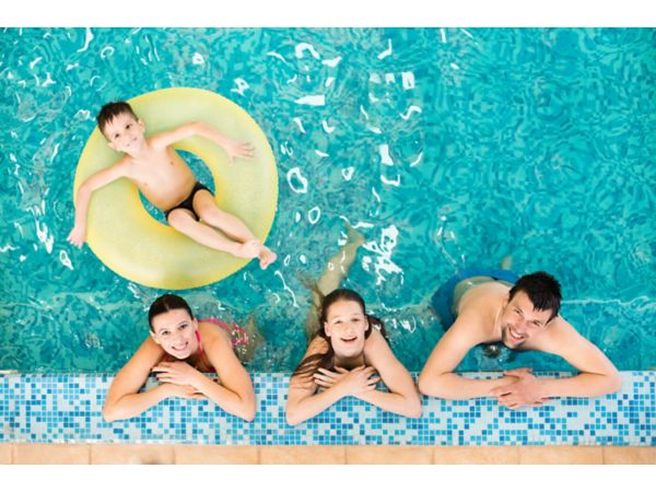 Happy family relaxing at the edge of the swimming pool, little boy relaxing on inflatable ring.