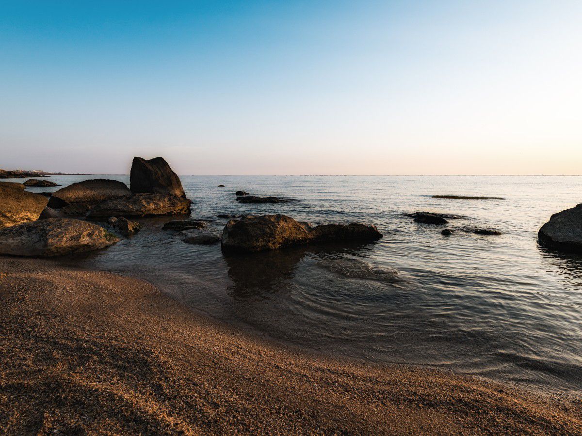 Rocky beach with calm ocean waters at sunset.