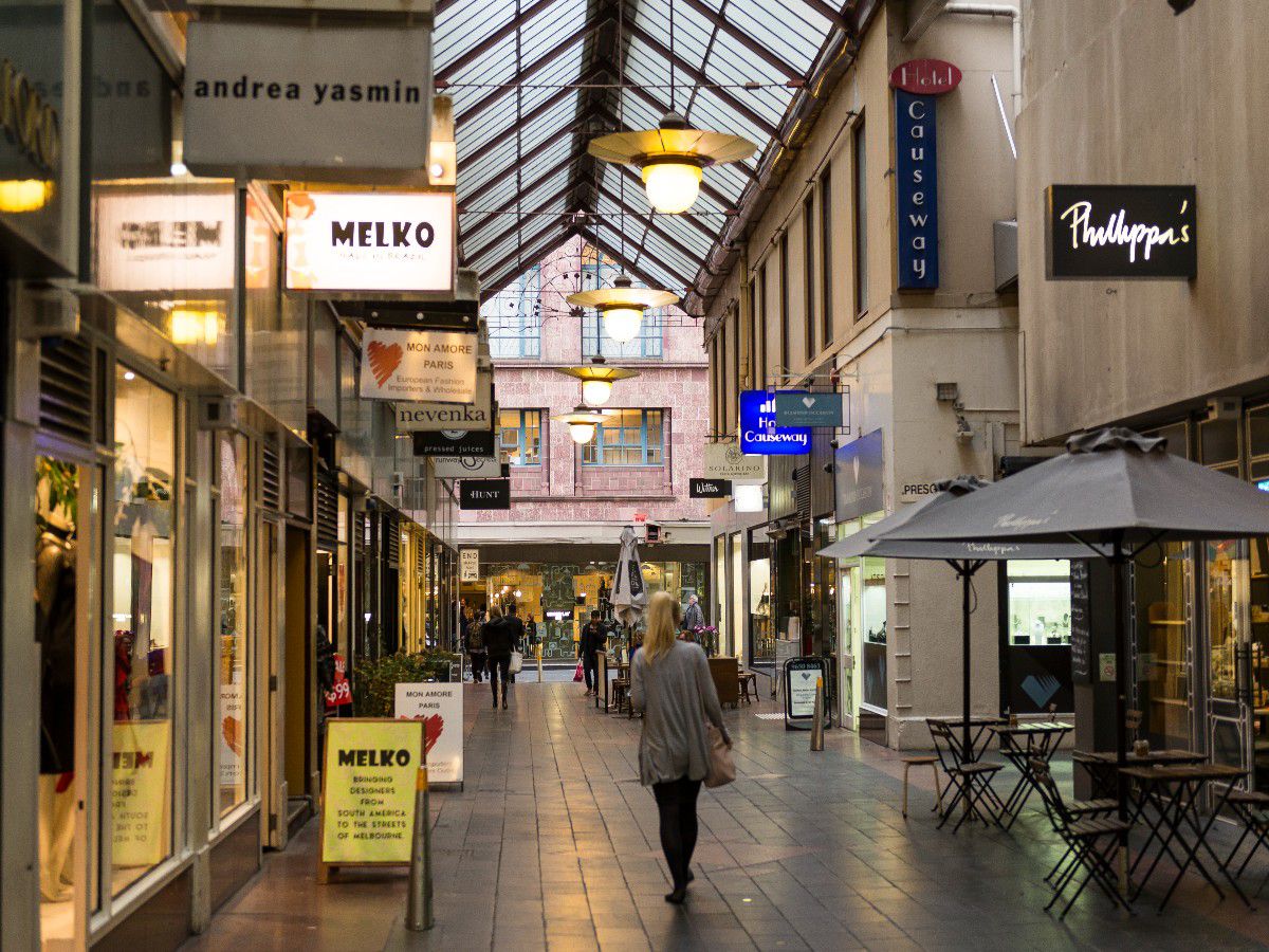 Covered shopping arcade with storefronts and pedestrians.