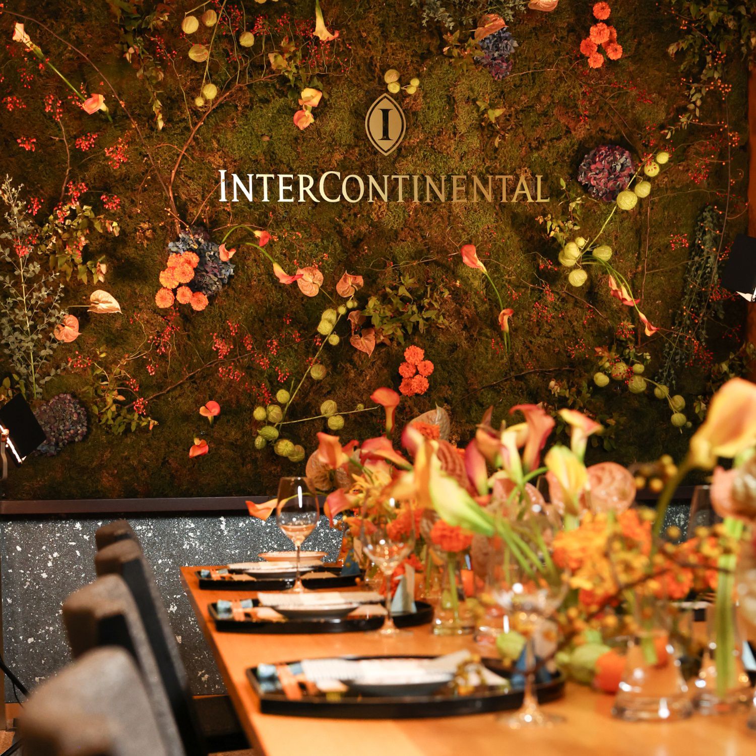 Elegantly set dining table in front of a mossy floral wall with the InterContinental logo.