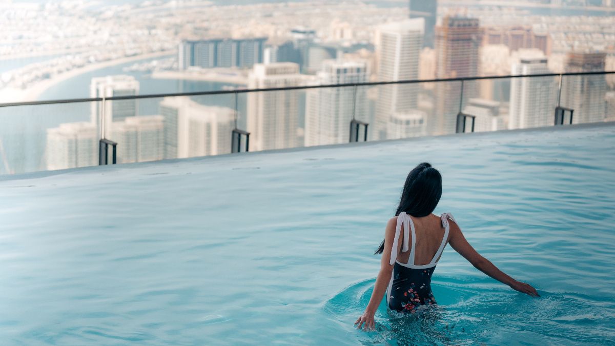 Woman swimming in an infinity pool overlooking city skyline.