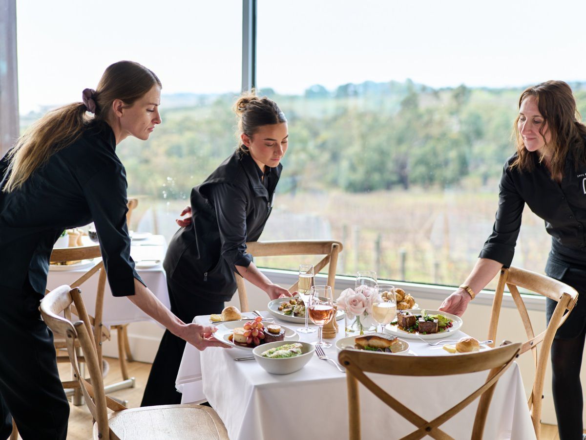 Three staff members arranging food on a restaurant table.