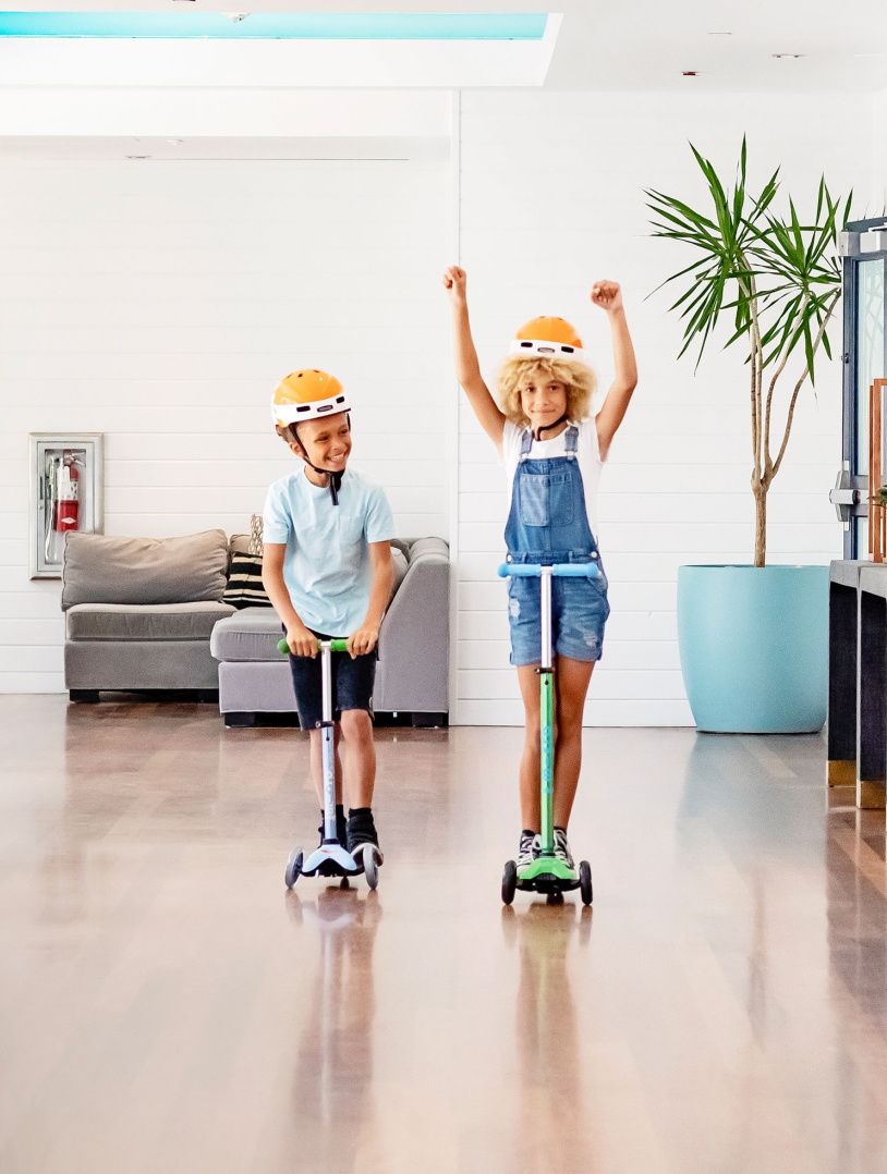 two kids riding scooters inside a lobby