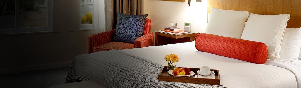 Hotel room view of queen bed with a tray of food
