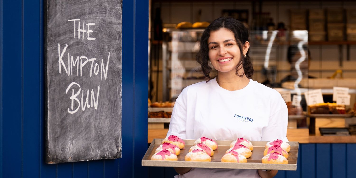 Woman holding a tray of baked goods - The Kimpton Bun