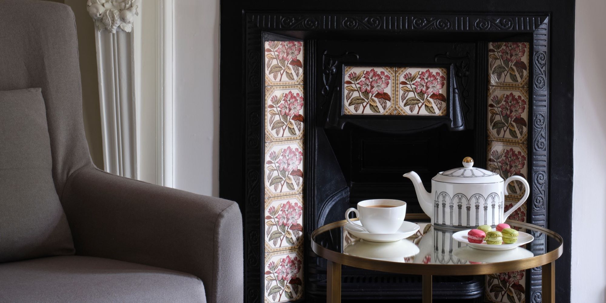 Teapot, a cup of tea, with green and pink macaroons in front of a fireplace