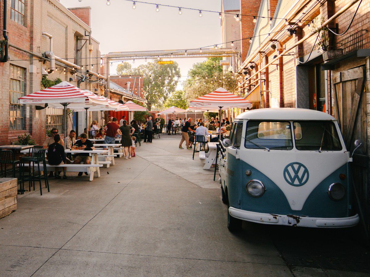 Outdoor brewery courtyard with vintage van and picnic tables.