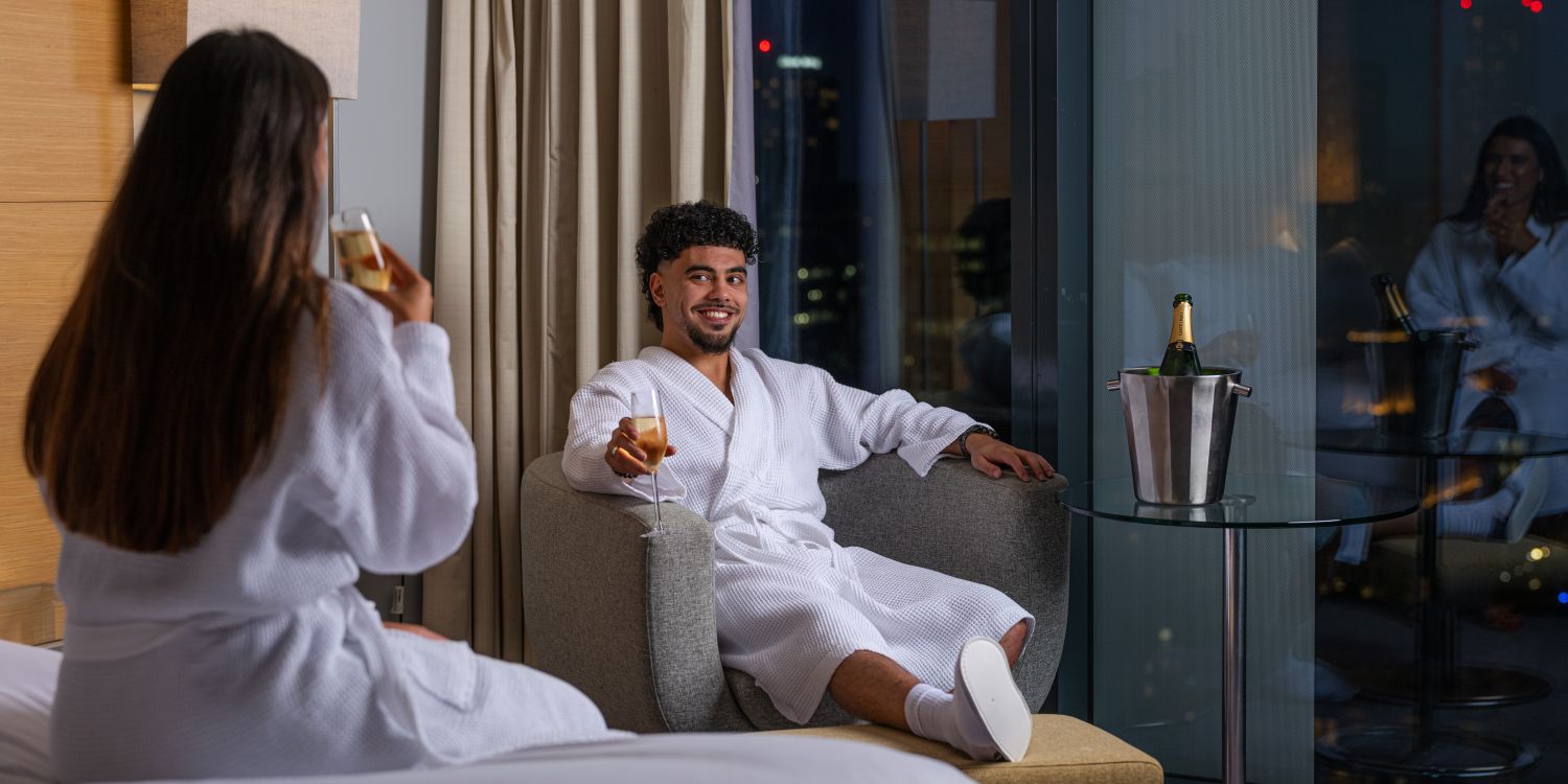 couple relaxing in hotel room in dressing gowns with prosecco