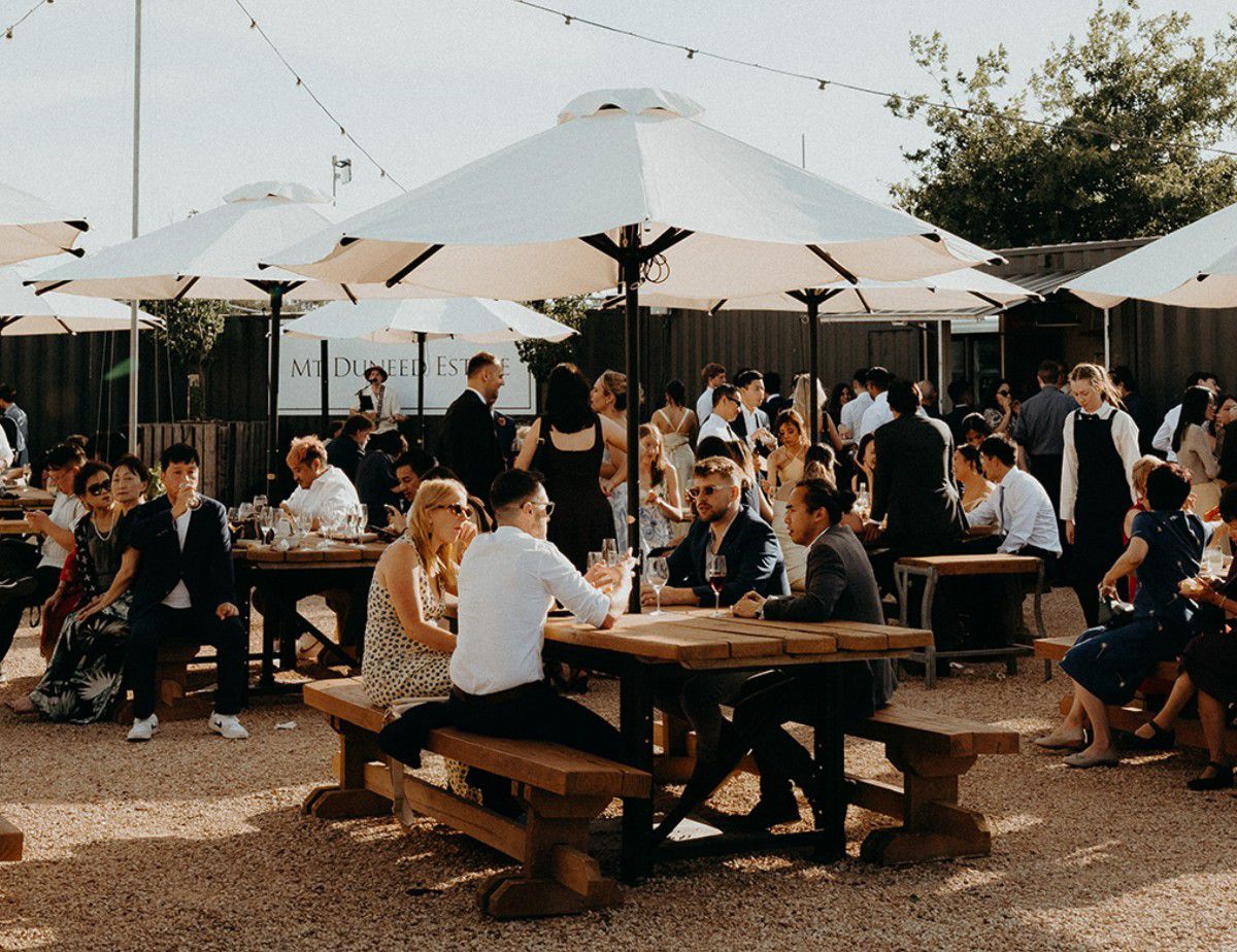 Outdoor estate dining area with people seated under umbrellas.
