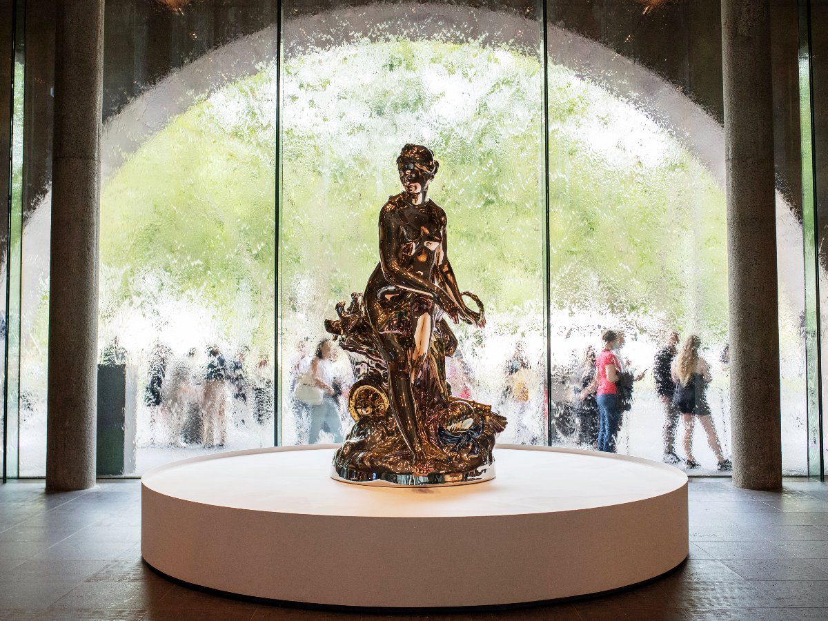 Bronze sculpture displayed before a large window.