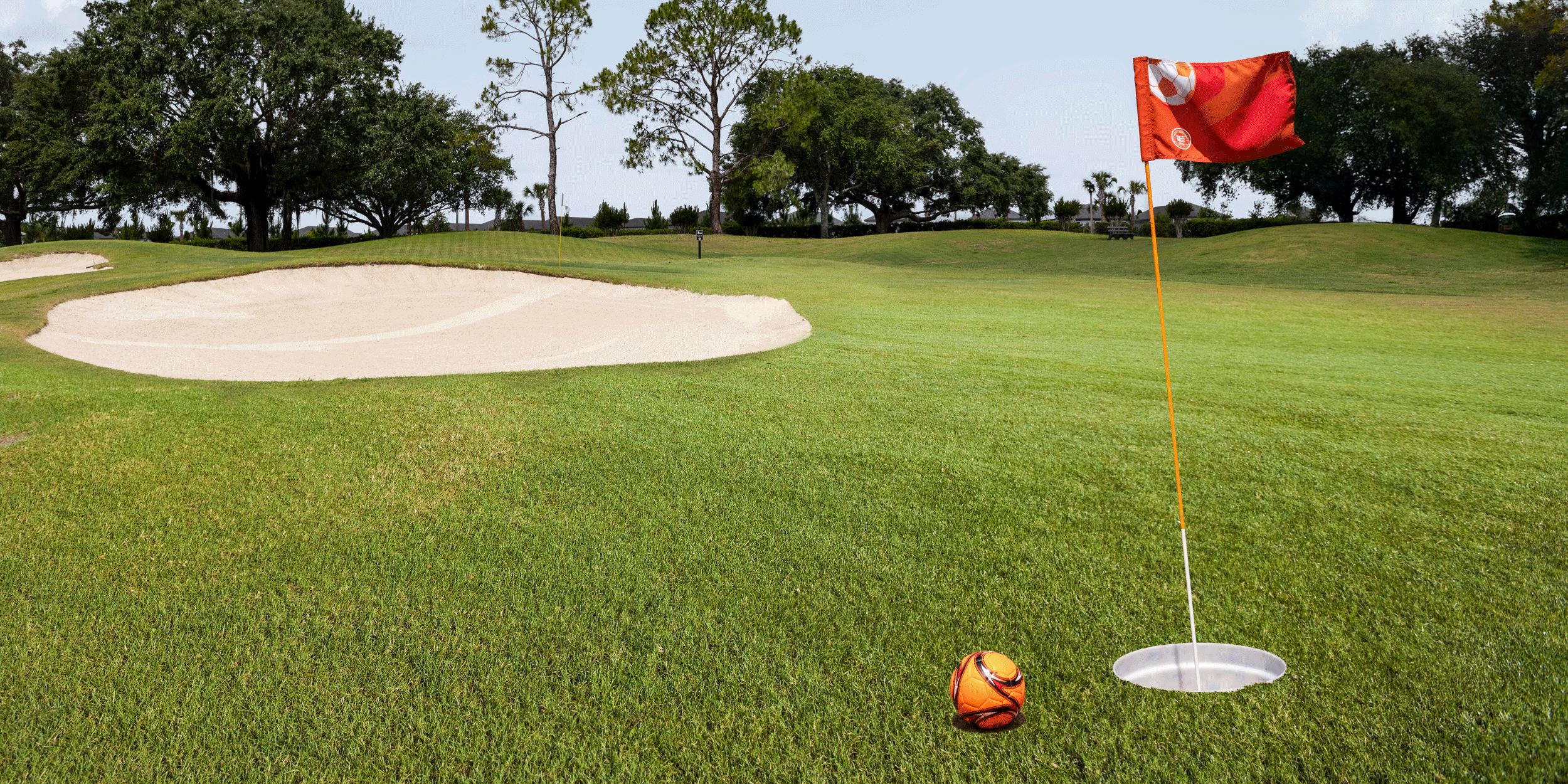 Soccer ball beside golf hole and flag on green fairway