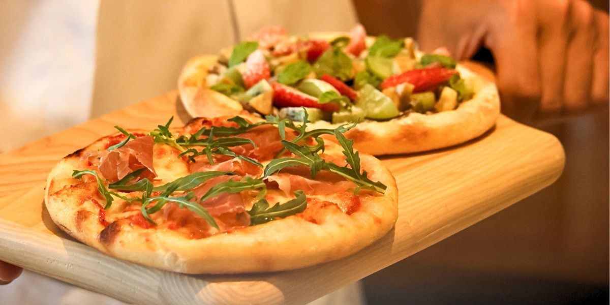 Two pizzas on wooden serving board at restaurant