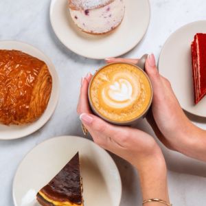 Hands holding latte surrounded by pastries and desserts