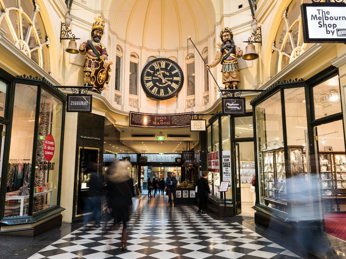 Historic arcade interior with shops, clock, and pedestrians.
