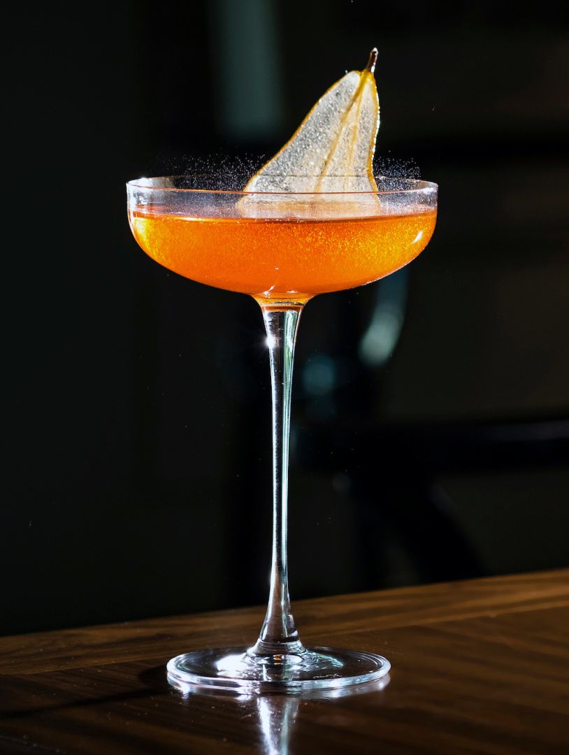 stemware with cocktail fizzing and thin sliced pear garnish