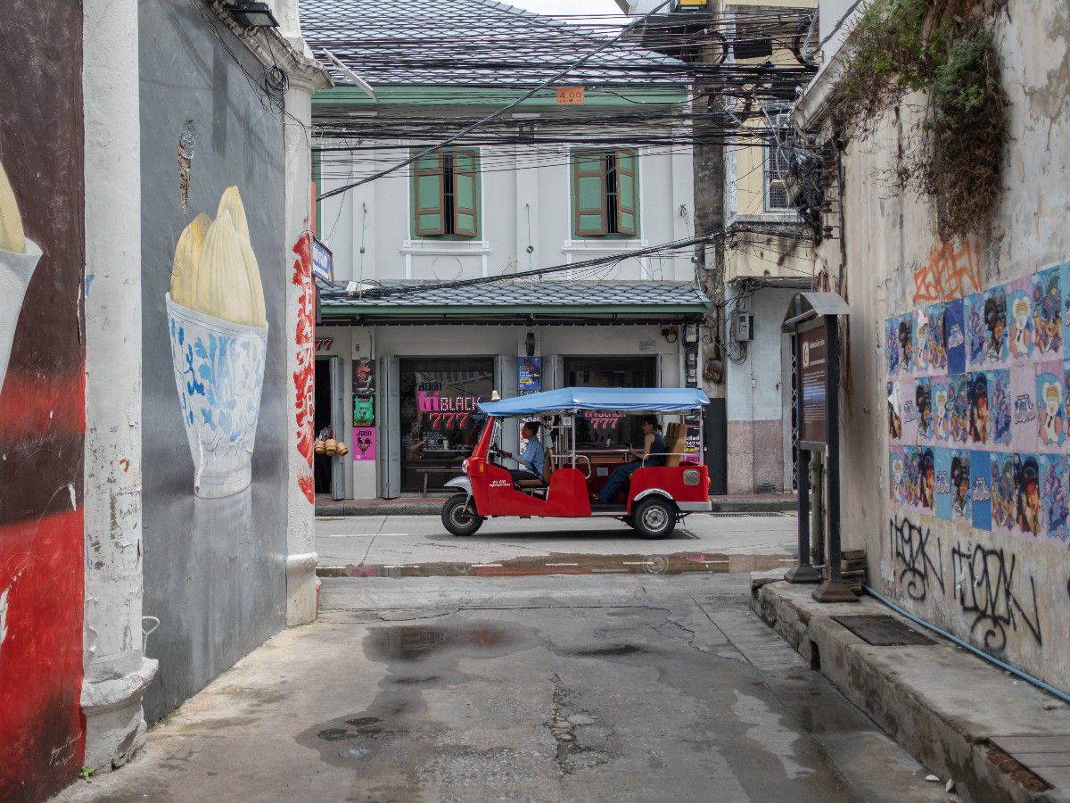 Street alley featuring colorful murals and a passing tuk-tuk.