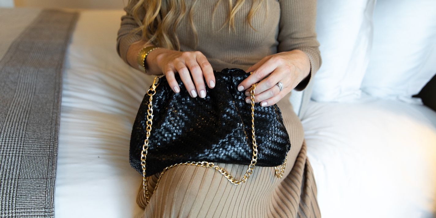 Hotel guest sitting on bed holding purse