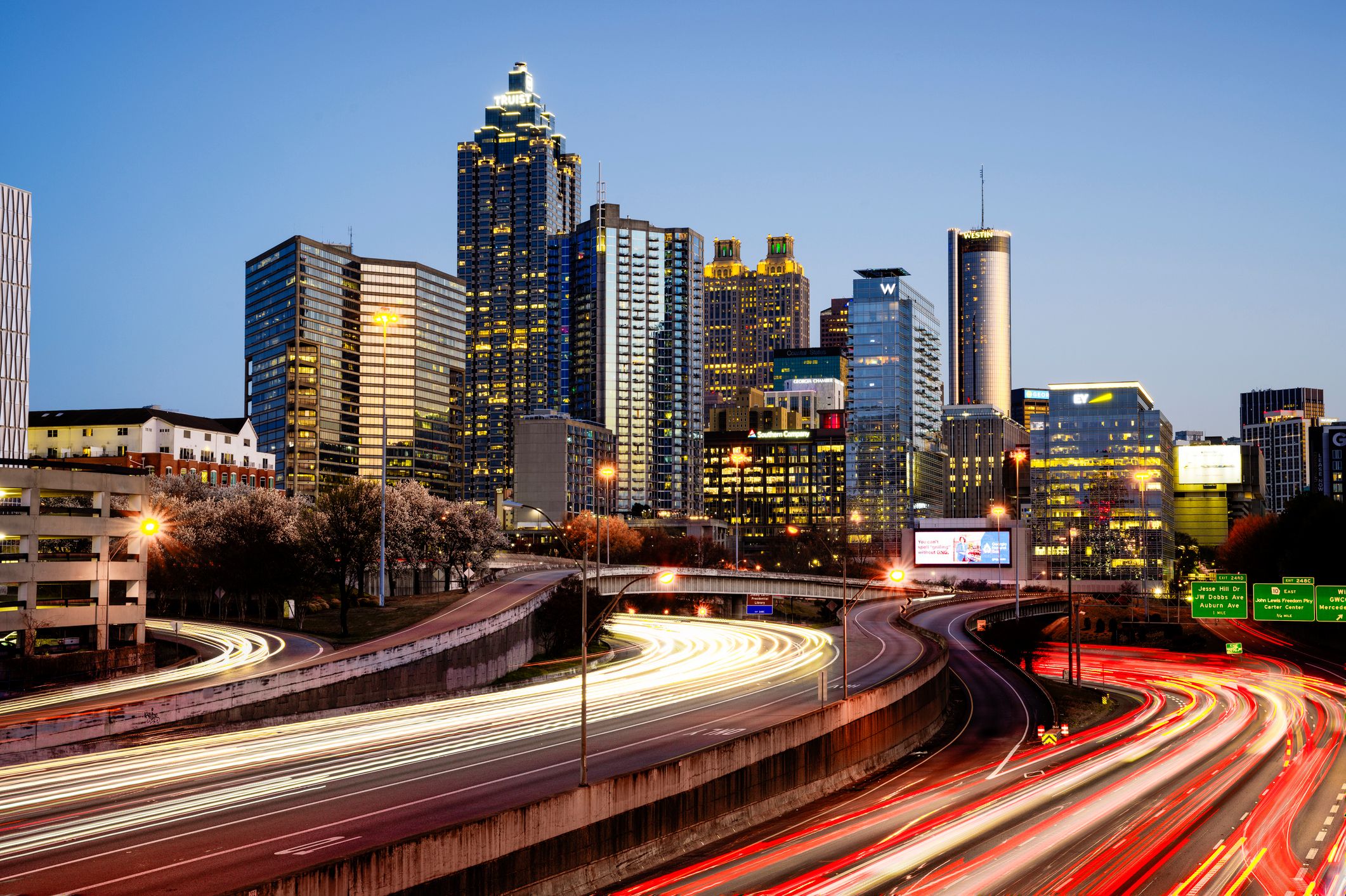 A vibrant cityscape of the Atlanta skyline captured at dusk, featuring illuminated skyscrapers and dynamic light trails from moving traffic. This stunning urban photograph highlights the energy and beauty of Atlanta, Georgia, during twilight, perfect for projects related to travel, city life, or modern architecture.