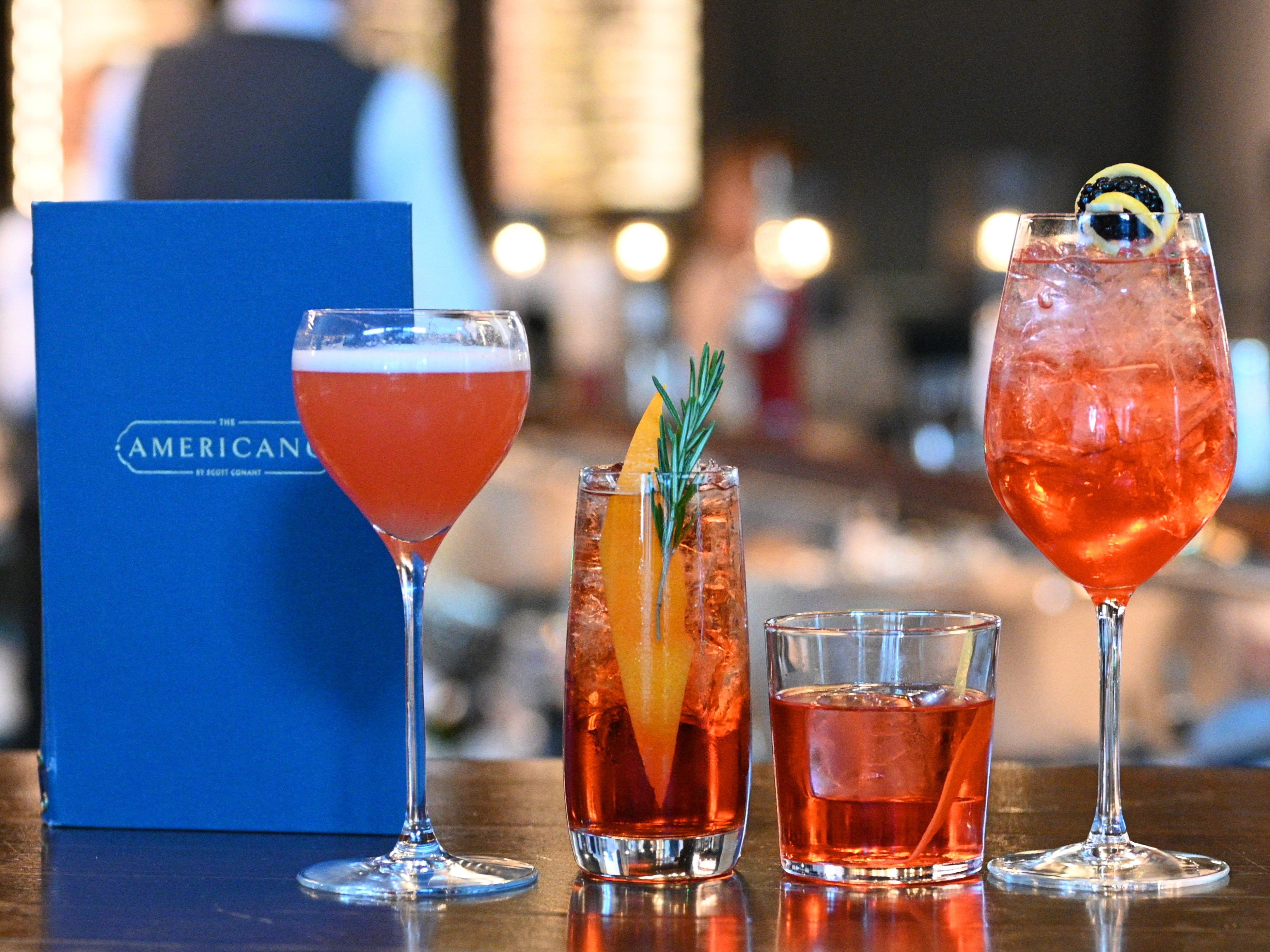 Four pink cocktails in assorted glassware on a bar next to an Americano menu.