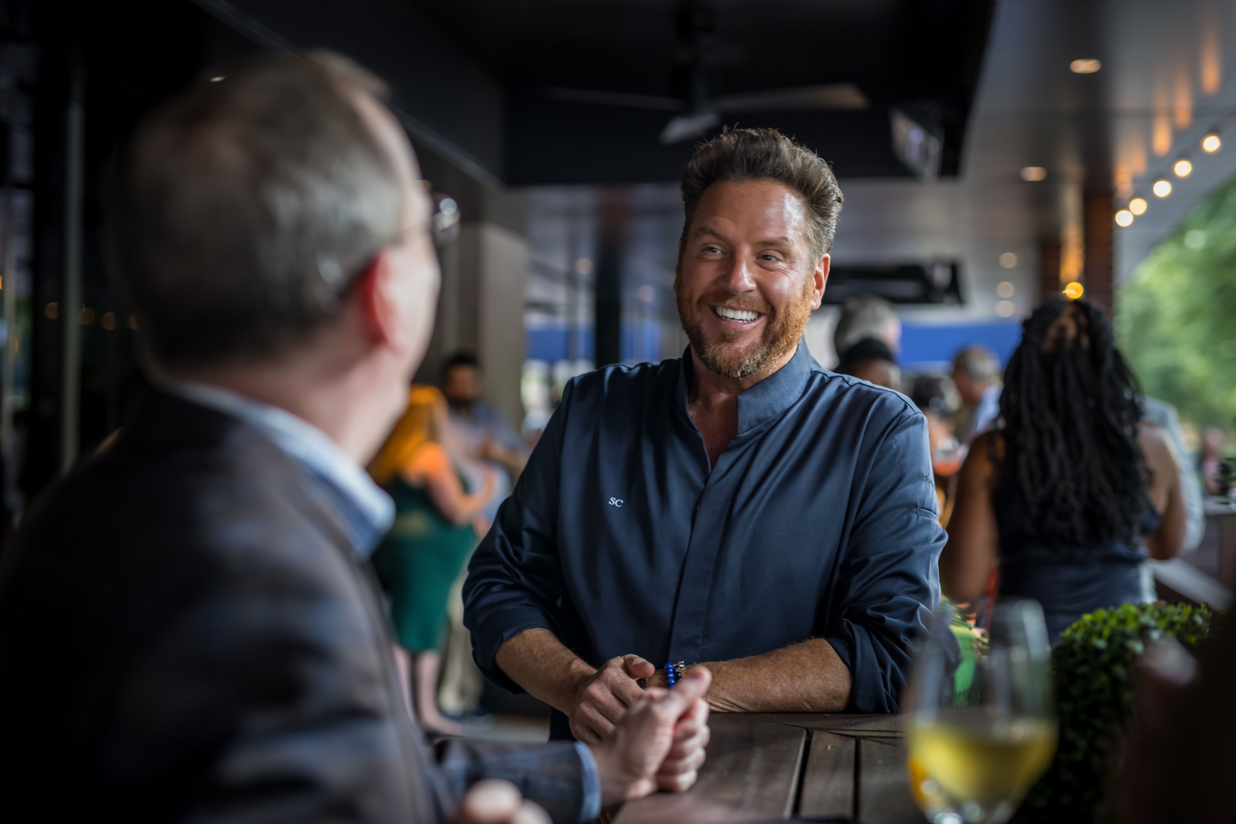 Chef Scott Conant talking to dining guests in a patio