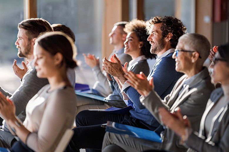 Attendees seated at a conference event applauding during a presentation.