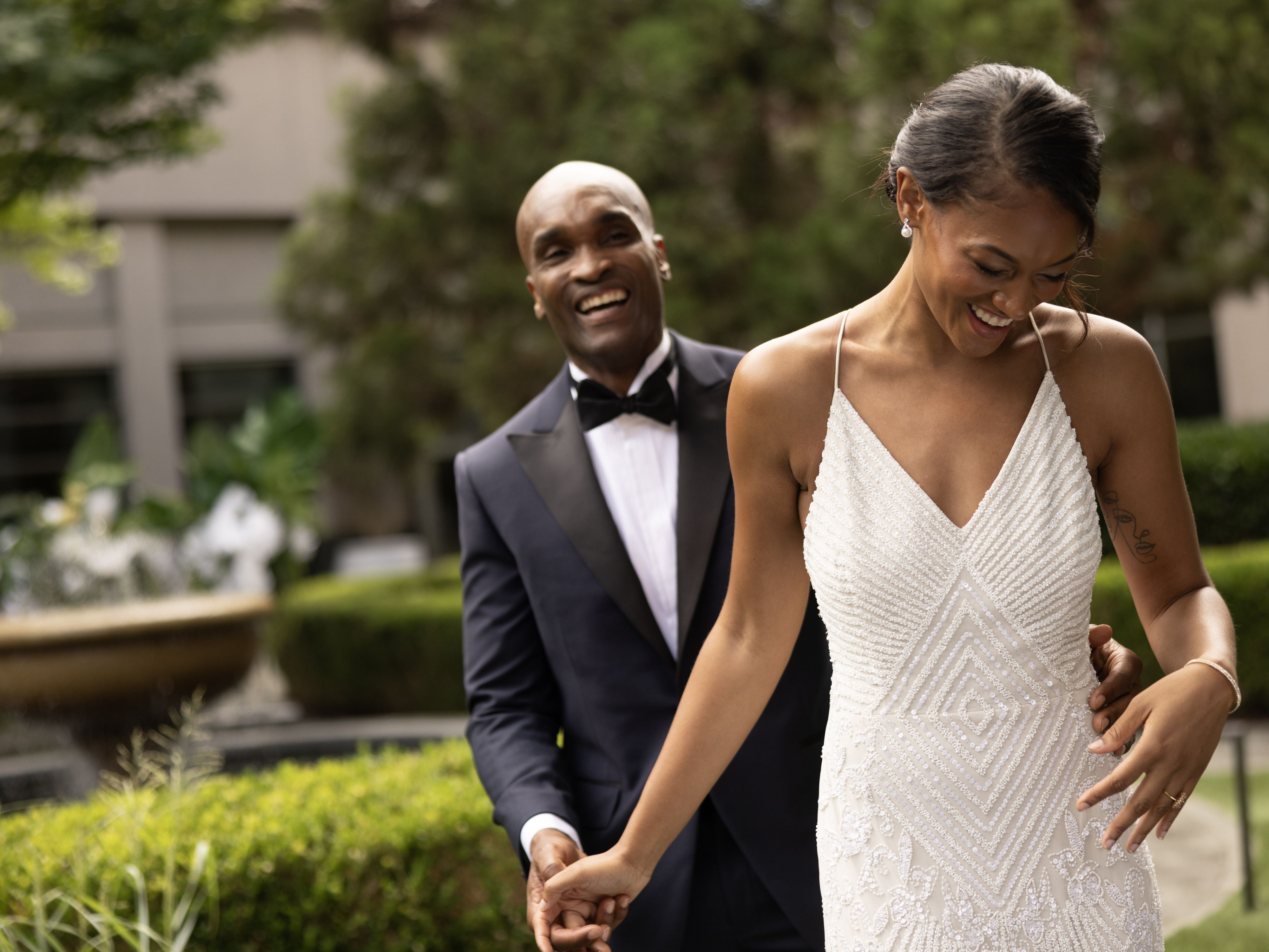 A married couple holding hands and walking through a garden after their wedding ceremony.