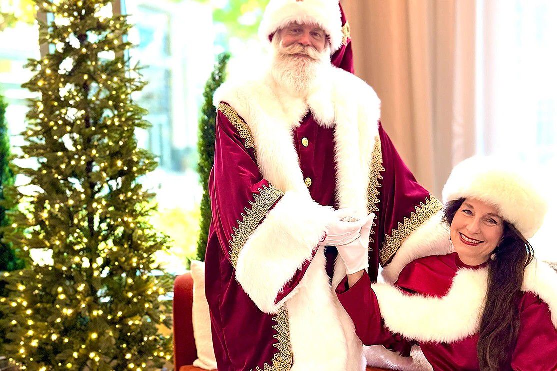 Santa and companion in festive red attire beside a decorated Christmas tree