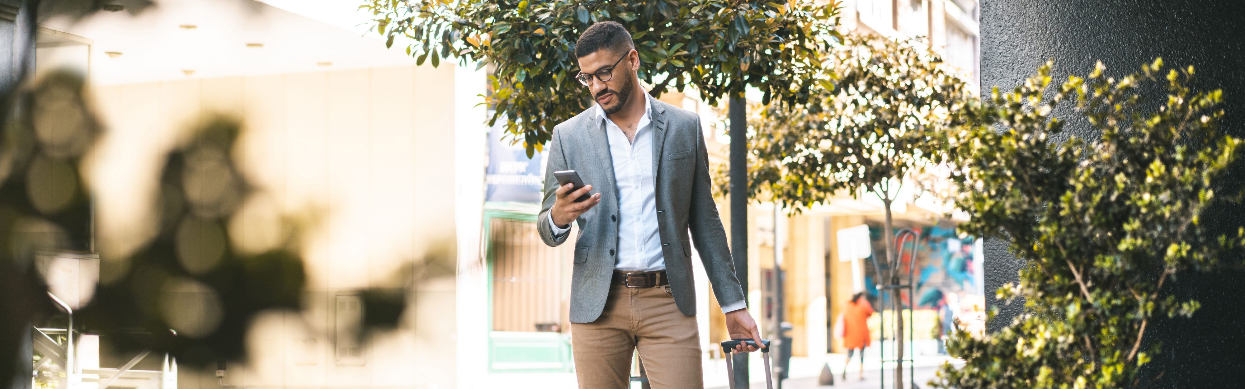 man in business attire walking with his phone and suitcase
